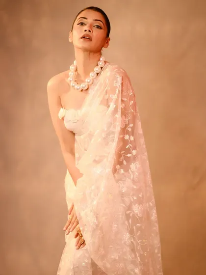 A high-fashion studio portrait where the subject's pose and the elegant drape of the sheer saree create a strong, statuesque look. The clean, minimal background and focused lighting draw all attention to the form and texture of the outfit, perfect for editorial or designer lookbooks.