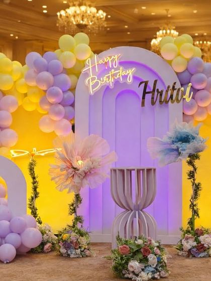 A stylish and modern first birthday setup for Hritvi. This party uses a soft pastel palette of yellow and lilac, with abstract floral elements and a neon sign for a chic and elegant look.