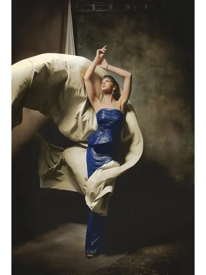 A dynamic shot for Ambika Lal, where a flowing fabric interacts with the model in a shimmering blue gown. This image combines stillness and movement to create a sense of high-fashion energy.