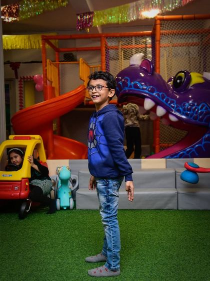 A happy boy posing in our play area, with the toy car and dragon slide visible in the background, showcasing the variety of activities.