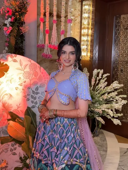 A vibrant and fun Mehendi look. The bride's hair is styled in a playful, textured braid that complements her colorful outfit and the festive atmosphere.