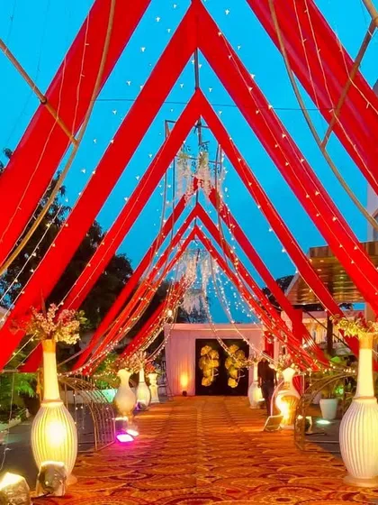 An outdoor entrance defined by bold red fabric drapes forming a triangular tunnel. This design is simple yet powerful, creating a striking visual against the evening sky.