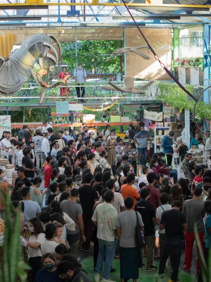 This is what community looks like. A wide shot of our bustling market inside the transformed warehouse, filled with people, plants, and art. This is the heart of what we do: bringing people together in a vibrant, sustainable space.