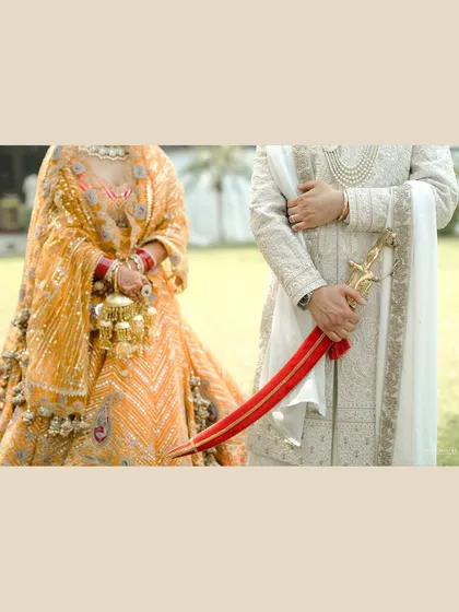 A detail shot focusing on tradition and style. This image captures the bride's kalire and the groom's kirpan, symbolic elements of a Sikh wedding, alongside their beautifully coordinated and textured outfits.