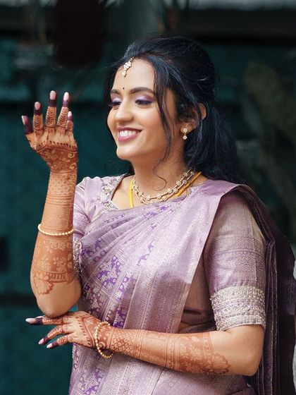 A radiant bride in a lavender saree, her smile and her beautiful mehendi lighting up the frame.
