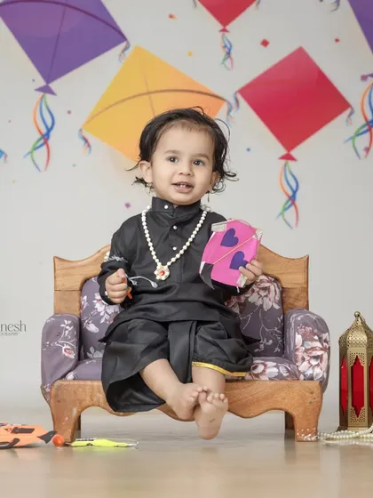 A classic Makar Sankranti portrait with a baby boy in a black kurta, holding a small kite. The backdrop is decorated with colorful kites, perfectly capturing the theme of the festival.