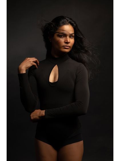 A minimalist and contemplative fine art portrait. The simple black bodysuit and dark background, combined with the motion of the hair, create a sense of quiet introspection.