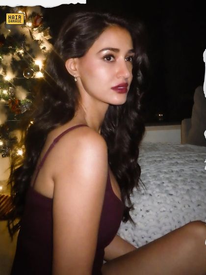 A festive shot with a Christmas tree in the background. The makeup features a classic bold red lip, perfect for any holiday party or special occasion.