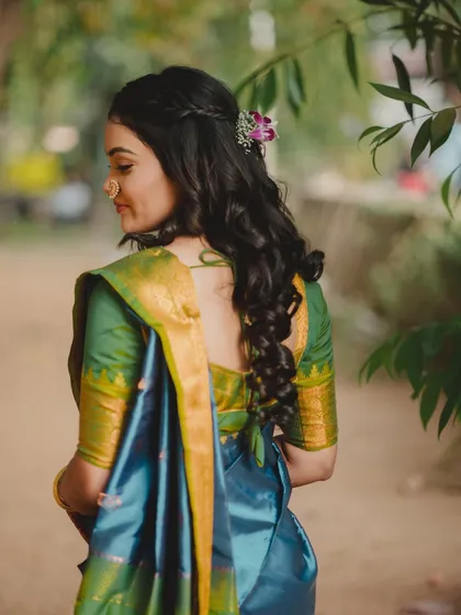 A beautiful shot of the bride from behind, showcasing her intricate hairstyle with a flower accent and the rich fabric of her saree. It's a portrait that focuses on elegance and detail.