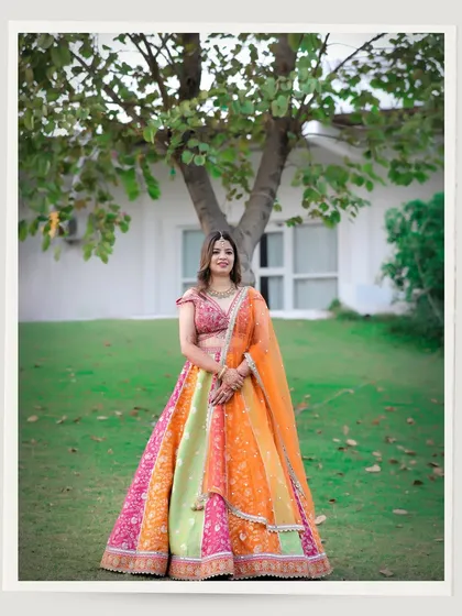 A beautiful solo portrait of the bride in her stunning, multi-colored lehenga. This shot highlights her grace and the beauty of her outfit against a simple, natural backdrop.