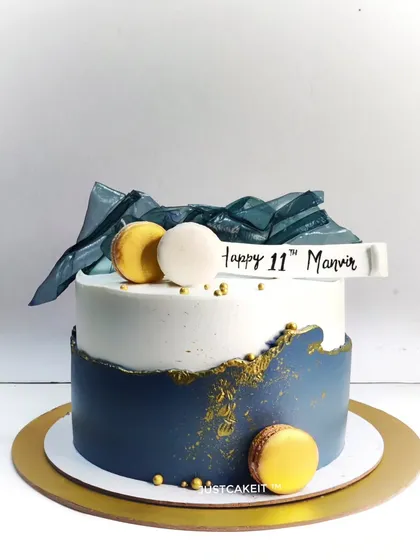 An abstract cake with a sophisticated navy blue and white color scheme. The design is accented with edible geometric sails and macarons.