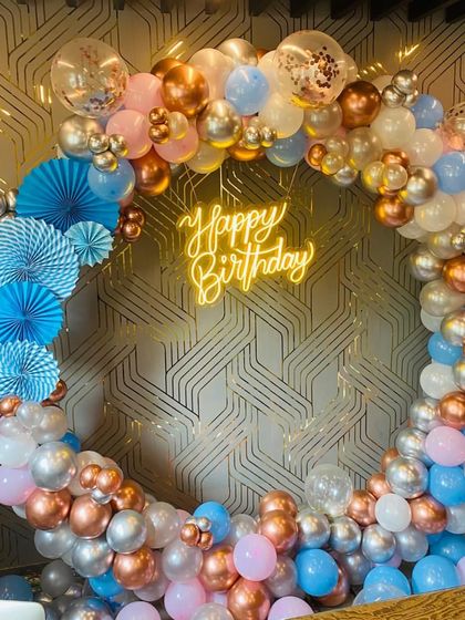 A unique birthday ring with blue, pink, rose gold, and silver balloons, accented with blue paper fans.