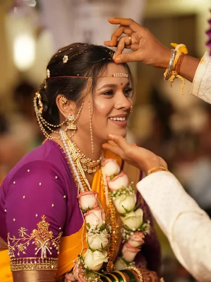 A beautiful ritual moment. The bride's happy expression and radiant makeup shine through as the sindoor is applied.