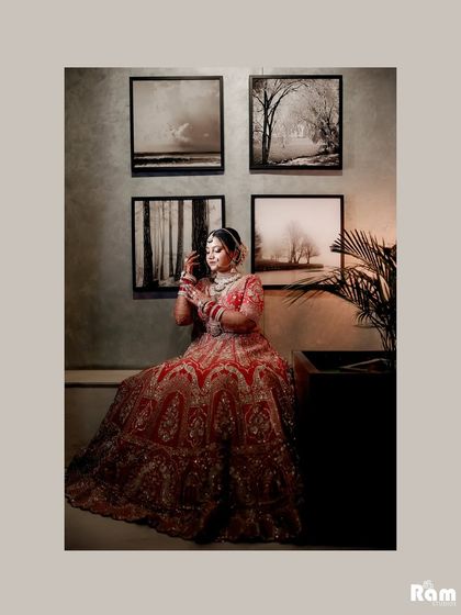 A serene portrait of the bride seated, her beautiful red lehenga contrasting with the minimalist art on the wall behind her.