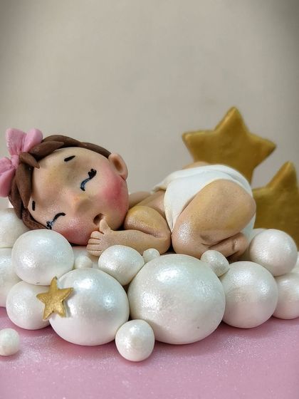 A close-up of the adorable sleeping baby topper from the pink christening cake, resting on a bed of shimmering, edible pearls.