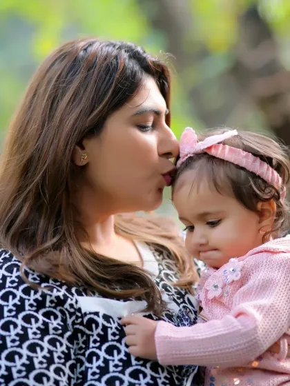 A sweet kiss from mother to daughter during an outdoor photoshoot. The natural light and green background create a soft and loving portrait.