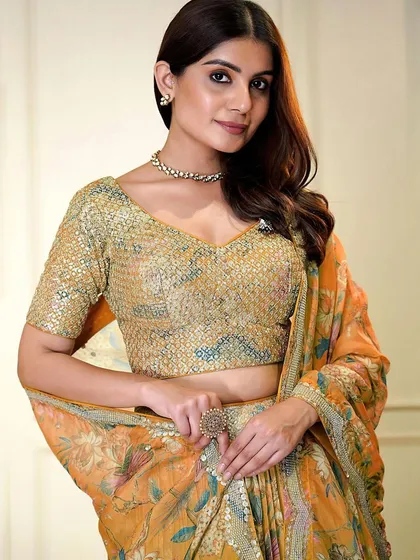 A pop of color for your celebration. This orange organza lehenga with a sequined blouse and floral skirt is designed for a fun and festive event like a Haldi or Sangeet.