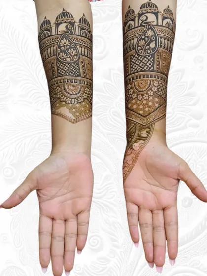 A full view of an elegant engagement mehendi, showcasing architectural domes and peacock motifs on the arms.