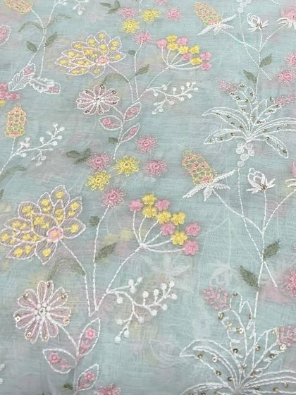 This pastel blue Mul Chanderi is covered in a whimsical floral and vine embroidery. The mix of yellow, pink, and white threads creates a cheerful and airy design perfect for a summer suit or dress.
