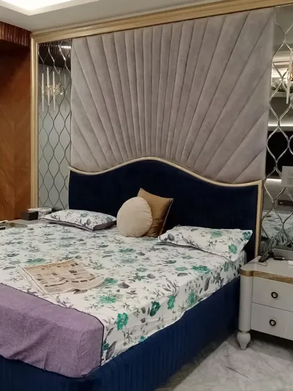 An elegant bedroom design featuring a custom headboard with radiating grey velvet panels and a deep blue base. Mirrored side panels with a geometric lattice design add a touch of glamour and visually expand the space.
