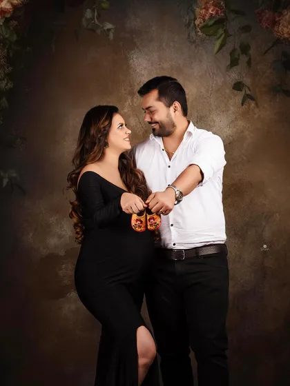 A classic couple's pose for an announcement. Holding up tiny baby shoes is a timeless way to share the happy news, captured here in a sophisticated studio setting.