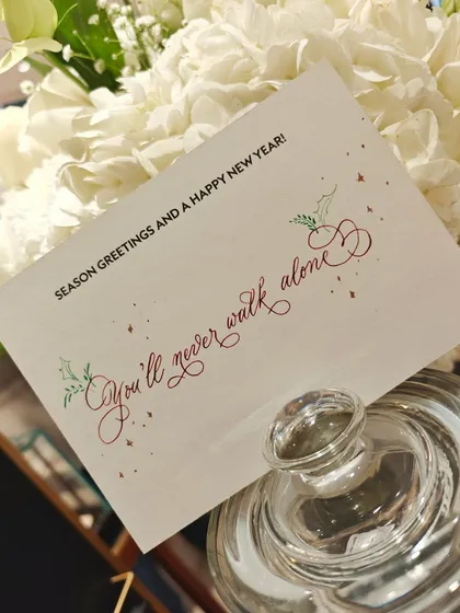 "You'll never walk alone." A season's greeting card with a heartfelt message, penned in calligraphy with small, festive holly illustrations. A December to remember.