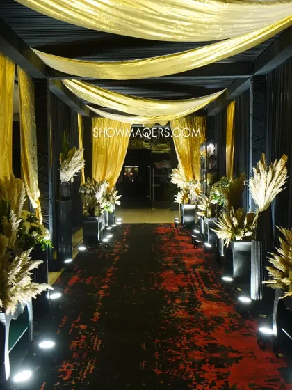 The dramatic black and gold walkway, lined with illuminated pampas grass, leading guests into the masquerade ball.
