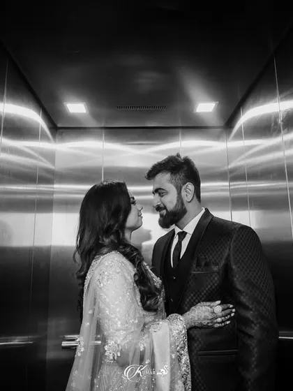 A black and white photo of a couple looking at each other in an elevator, using the reflective surfaces for a modern, graphic composition.