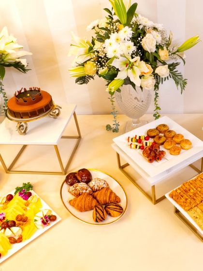 A wide view of the beautiful high-tea spread for L'Opéra. The table features a stunning cake, croissants, cheese boards, and canapés, all elegantly arranged with fresh flowers.