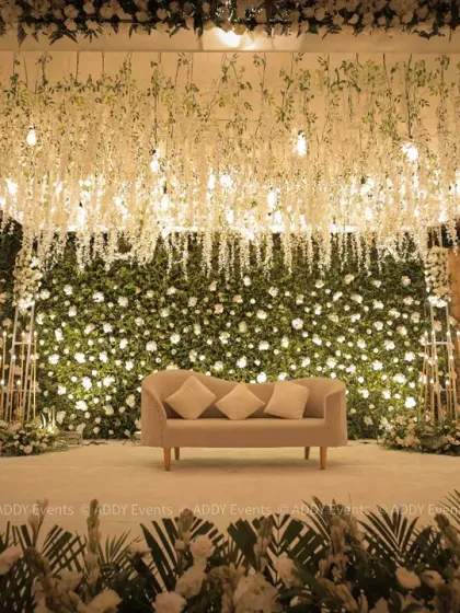 We design stages that serve as the elegant centerpiece for your most important occasions. This sophisticated setup features a lush wall of white and green florals, complemented by a ceiling of cascading wisterias and soft, ambient lighting, perfect for award ceremonies or executive galas.