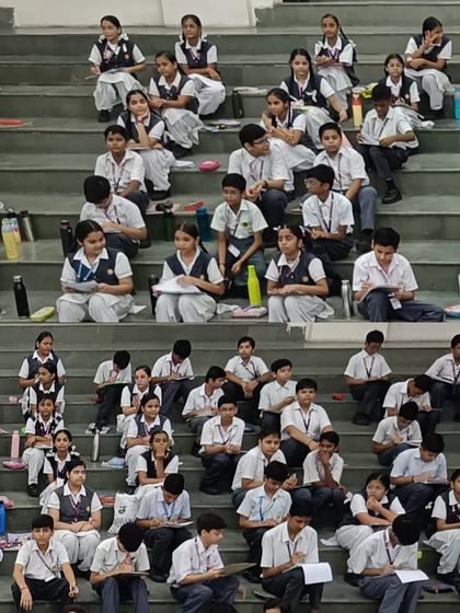 Students at Gayatri Public School during the 2024 Olympiad, seated on the steps of the auditorium, fully concentrated on their papers.