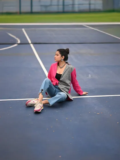A wide shot of a model on a tennis court, showcasing a unique pink and grey jacket. The unusual setting adds an element of surprise and modernity to the fashion shot.