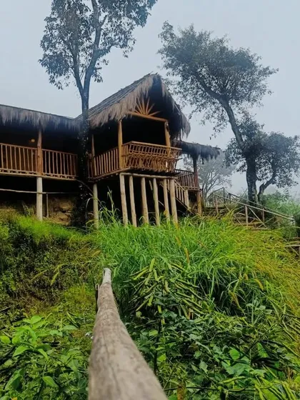 The beautiful mud house perched on the hillside, surrounded by lush greenery and misty views.