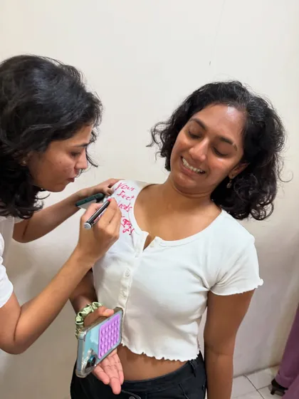 A student smiling through her "roast" as a friend writes a funny jab on her t-shirt. This is our unique way of celebrating Friendship Day, full of savage salsa shade and lots of love.