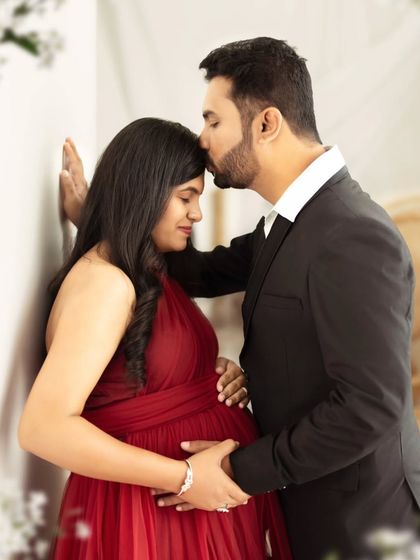 A tender forehead kiss, capturing a quiet and intimate moment between the expecting parents.