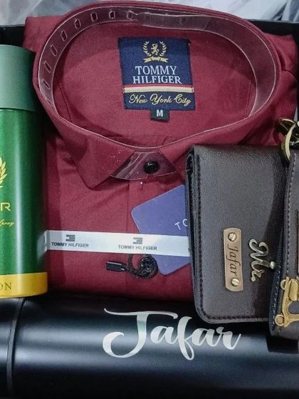 A rich maroon hamper with a Tommy Hilfiger shirt, a personalized wallet and keychain, and a name-engraved flask.