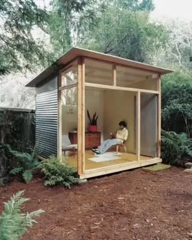 A minimalist tiny room with glass walls, perfect as a reading nook or meditation space in a garden. It's a simple structure that allows you to feel connected to nature.