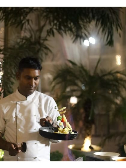 A chef artfully plates a stir fry dish in a small pan, ready to be served. This action shot, set against an outdoor backdrop, demonstrates the care and precision that goes into every single serving, even at a busy live station.