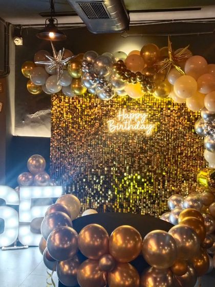 The 65th birthday setup illuminated, showing the vibrant shimmer wall and the warm glow of the neon and marquee lights.