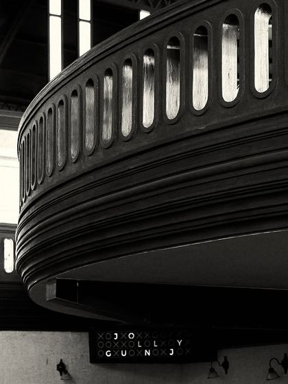 The heavy, dark wood of the balcony creates a strong visual anchor in the space. This view also captures a glimpse of an ornate mirror and wall sconces below.