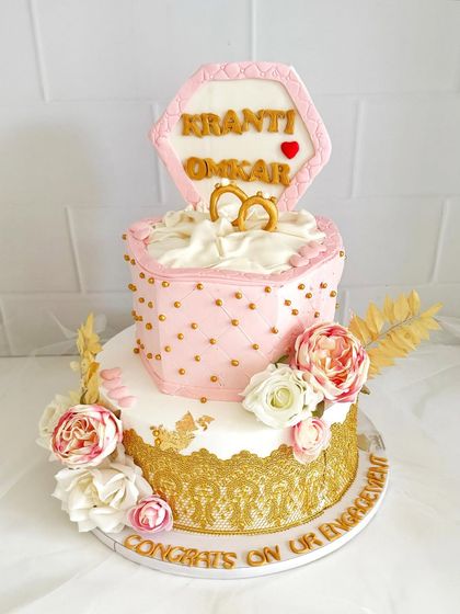 A truly unique engagement cake designed to look like a ring box. This two-tier creation features a quilted pink top tier, gold lace detailing, and beautiful floral accents.