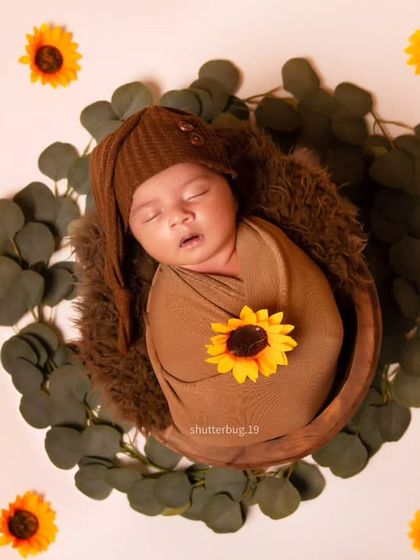 A simple and beautiful overhead shot. The baby is wrapped snugly in a basket, holding a single sunflower, and surrounded by scattered sunflower heads.