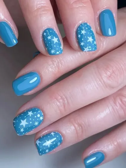 A celestial-themed design with a beautiful blue base and accent nails covered in a pattern of white stars.