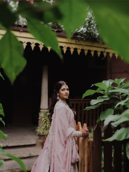 The bride looks back over her shoulder, framed by lush green leaves. This candid-style portrait captures a moment of quiet beauty in a natural, serene setting.