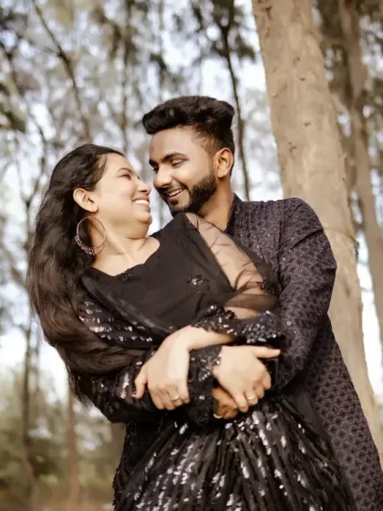 An embrace in the woods. The couple, dressed in black, shares a joyful and intimate moment during their pre-wedding shoot.