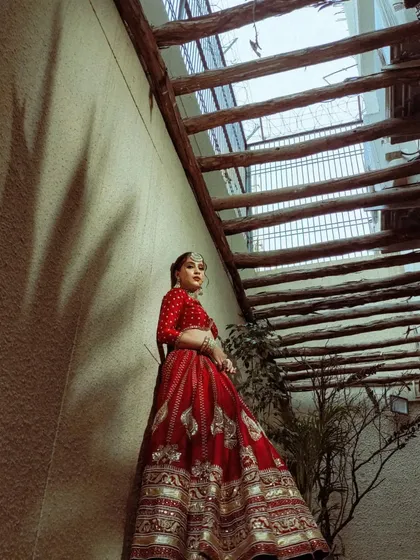 A full-length shot capturing the dramatic flair of the red lehenga. The pose and angle are chosen to highlight the beautiful embroidery on the skirt.