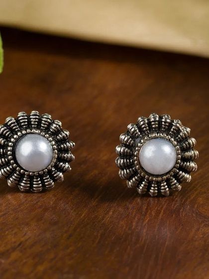 A pair of classic silver and pearl stud earrings on a dark wood background. The rustic styling gives these traditional earrings a timeless feel.