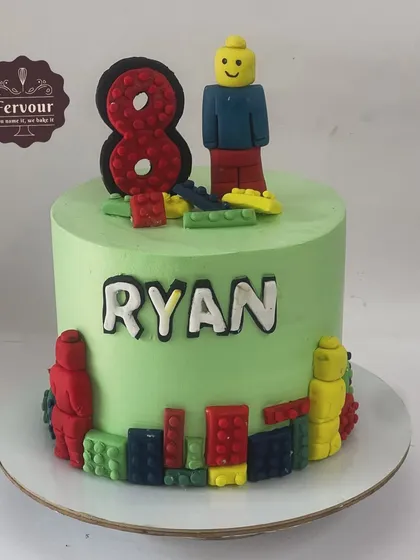 A Lego theme cake for an 8th birthday. This chocolate truffle cake is covered in green whipped cream and decorated with hand-crafted fondant Lego figures and blocks.