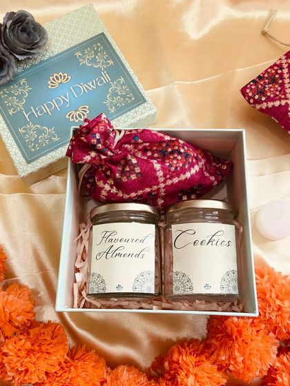 A simple and elegant Diwali gift box containing two jars of flavored almonds and cookies, along with a traditional bandhani potli for an ethnic touch.