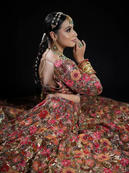 A back view of an intricate bridal hairstyle. This shot highlights the detailed work of the long braid, adorned with traditional parandi accessories, flowing down the model's back over a heavily embroidered lehenga.